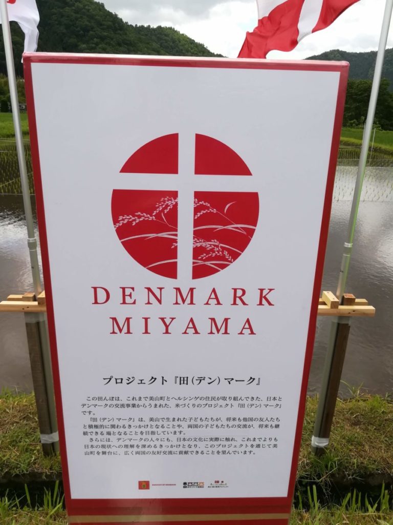 DENMARK MIYAMA プロジェクト 「田 (デン) マーク』 この田んぼは、これまで美山町とヘルシンゲの住民が取り組んできた。日本と デンマークの交流事業からうまれた、米づくりのプロジェクト「田(デン) マーク」 です。 「田(デン) マーク」は、美山で生まれた子どもたちが､将来も他国の友人たち 的に関わるきっかけとなることや、両国の子どもたちの交流が、将来も できる場となることを目指しています。 さらには、デンマークの人々にも、日本の文化に実際に触れ、これまでよりも 日本の現状へのきっかけとなり、このプロジェクトを に、広く両国の友好交流に貢献できることを望んでいます。