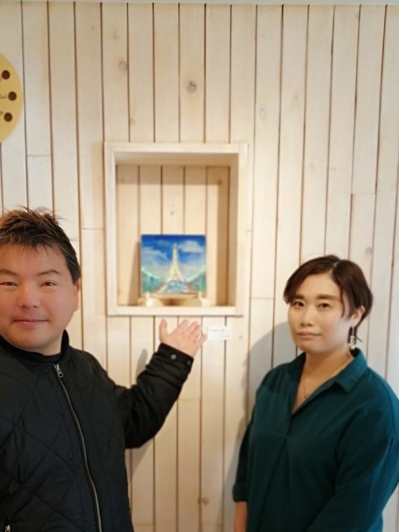 名古屋のアート空間スカーラでエッフェル塔を描いた絵画の前に立つ榊原平と宮地靖江さんの光景