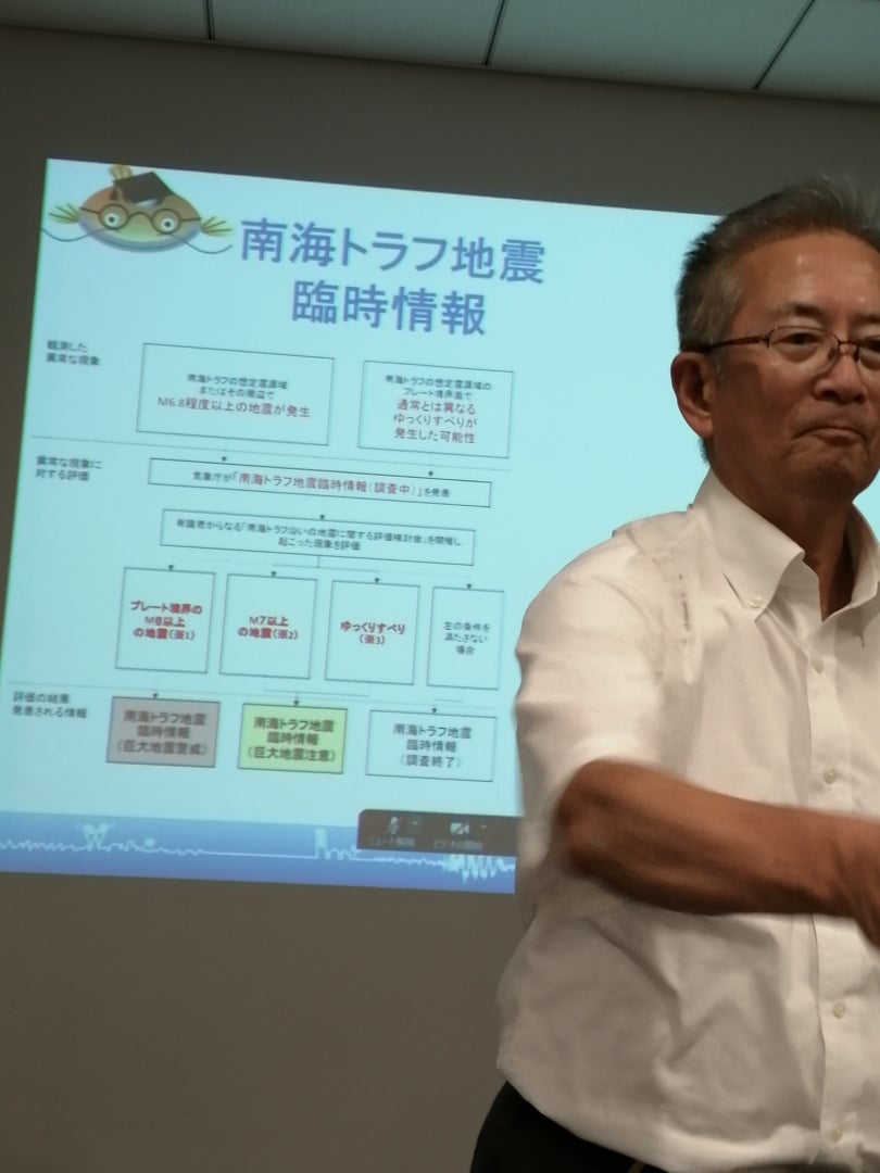 名古屋大学名誉教授 福和伸夫氏が、南海トラフ地震に関する臨時情報のフローチャートを示したスライドを背景に講演中。
