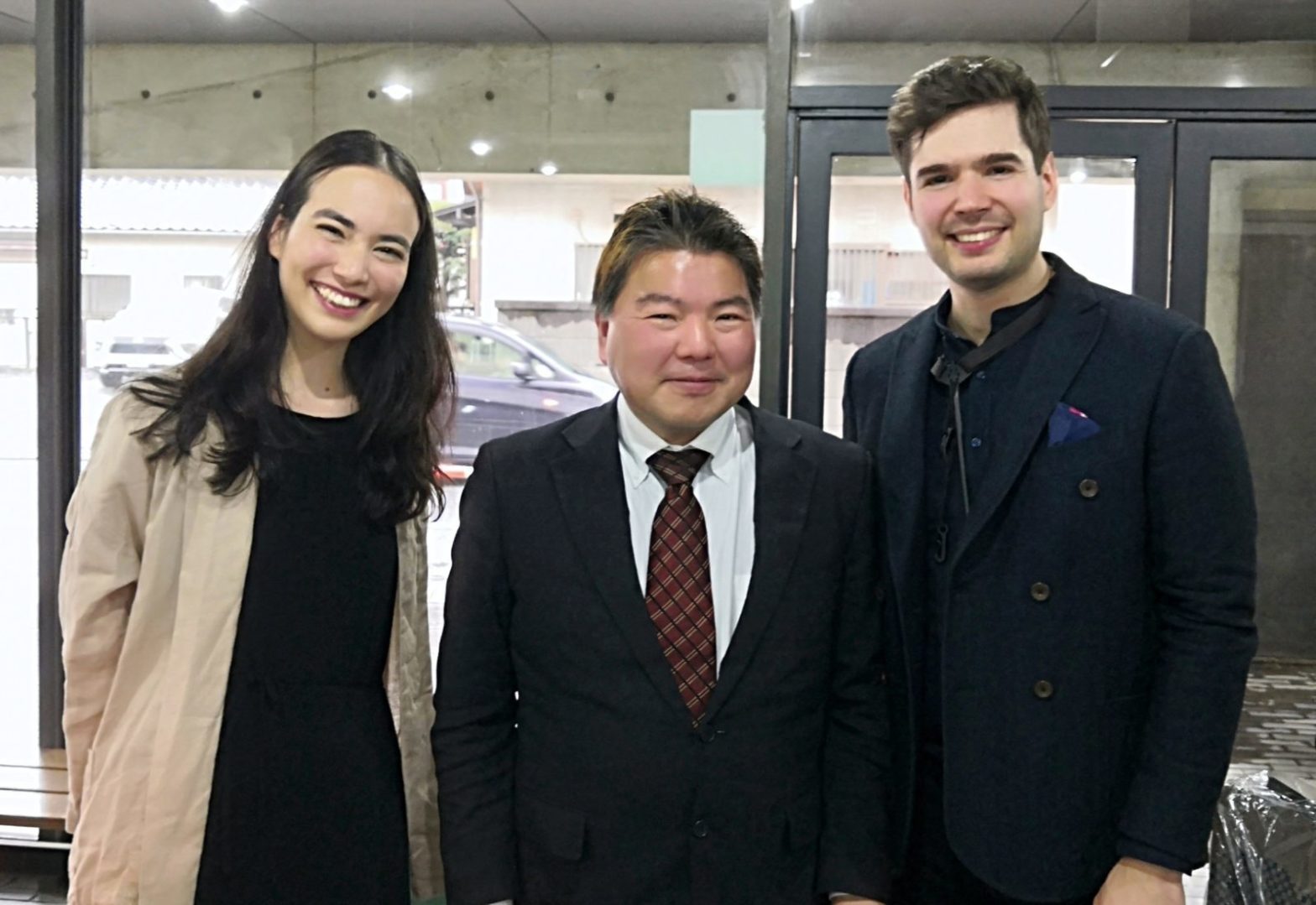 埼玉県富士見市 鶴瀬コミュニティセンターで、セルビア出身のサックス奏者マルコ・ジョンバさんとドイツ人のピアニストシルヴィア・季実子・クルツさん、そしてスーツを着た榊原平さんの3人が立っている光景です