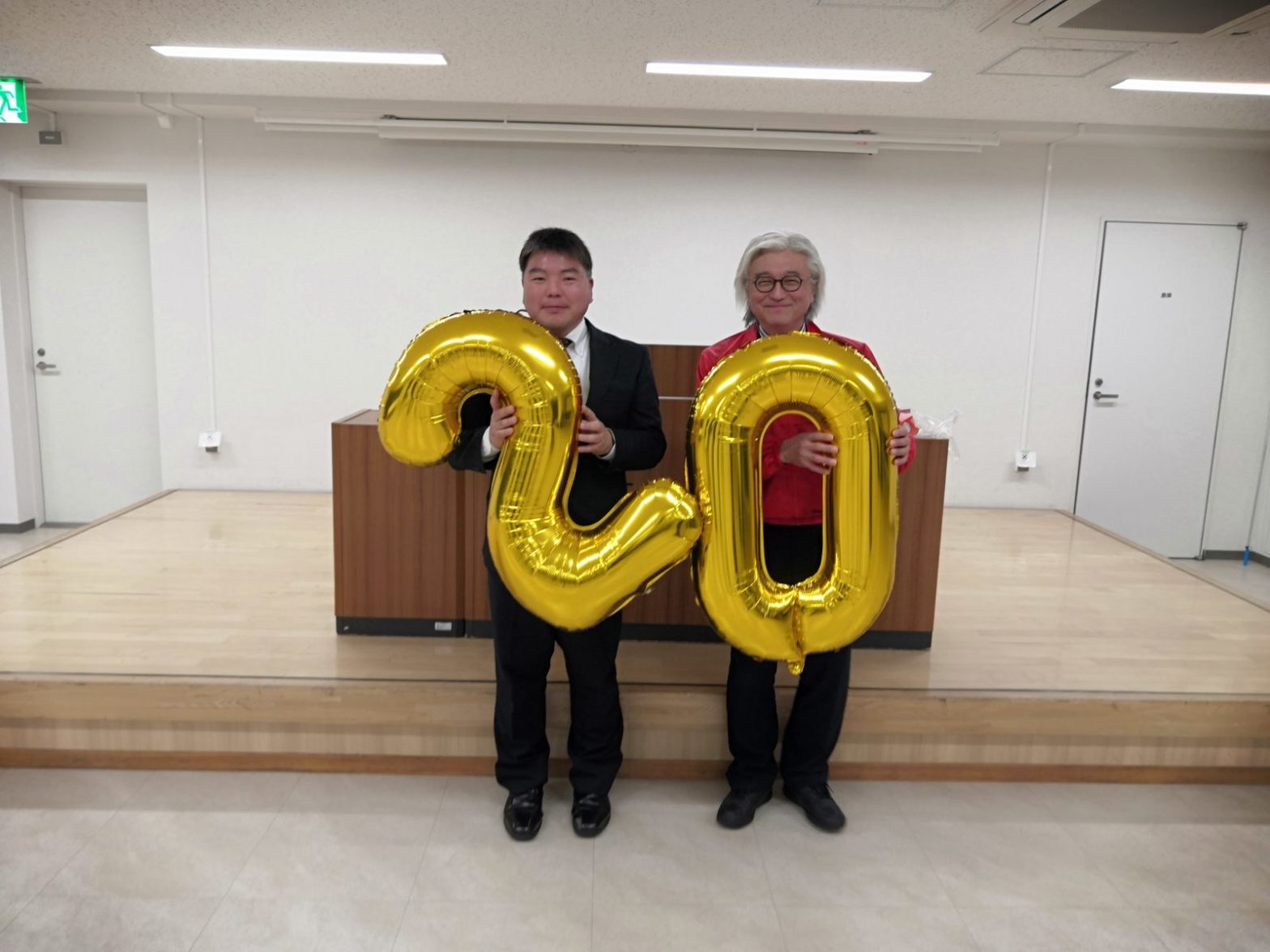 20周年記念の黄色いバルーンを持つ宿輪純一博士（経済学）と榊原平