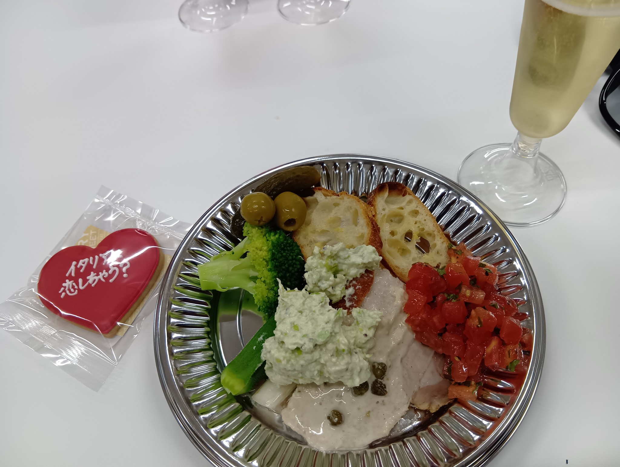 名古屋日伊協会 アペリティーボ 万博 富井貴子氏と語る2025年大阪・関西万博イタリア館の魅力 10 名古屋日伊協会 アペリティーボの料理。イタリア国旗の色を意識した盛り付けで、ハートのクッキーとオリーブオイルのボトル、スパークリングワインのグラスが写っている。