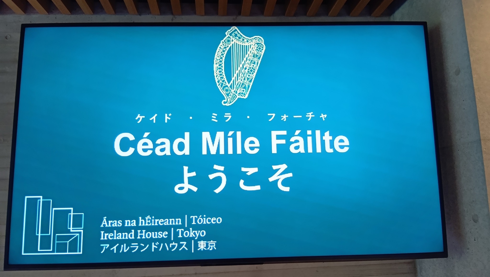 アイルランドハウス東京の館内にあるウェルカムサイン。青い背景に、アイルランドのハープの紋章と「Céad Míle Fáilte（ゲール語）」「ようこそ」「Ireland House | Tokyo アイルランドハウス | 東京」と白抜き文字で書かれている。