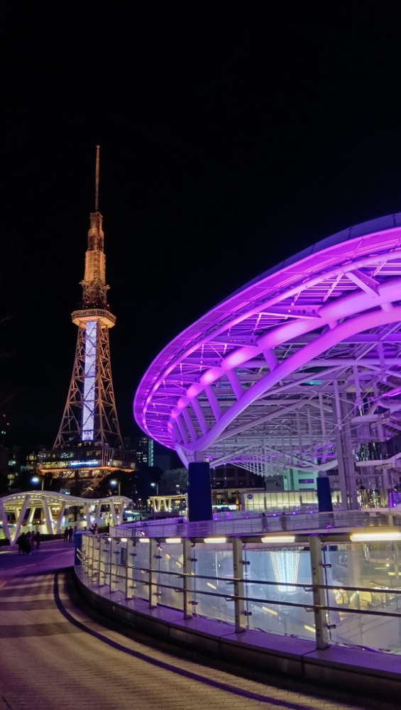 椙山フィルハーモニーオーケストラ 第58回定期演奏会 〜白い翼が響かせた歓喜と涙〜 2 夜の名古屋・栄の風景。ライトアップされた中部電力 MIRAI TOWER(旧名古屋テレビ塔)と、紫色に輝くオアシス21の「水の宇宙船」が写っている。